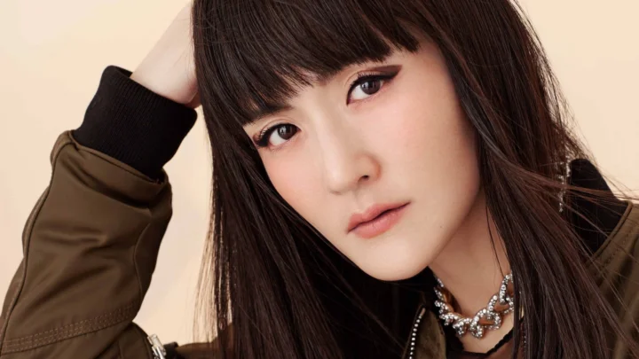 一名留着深色长发的女性身穿棕色夹克，以近距离肖像姿态面对镜头。