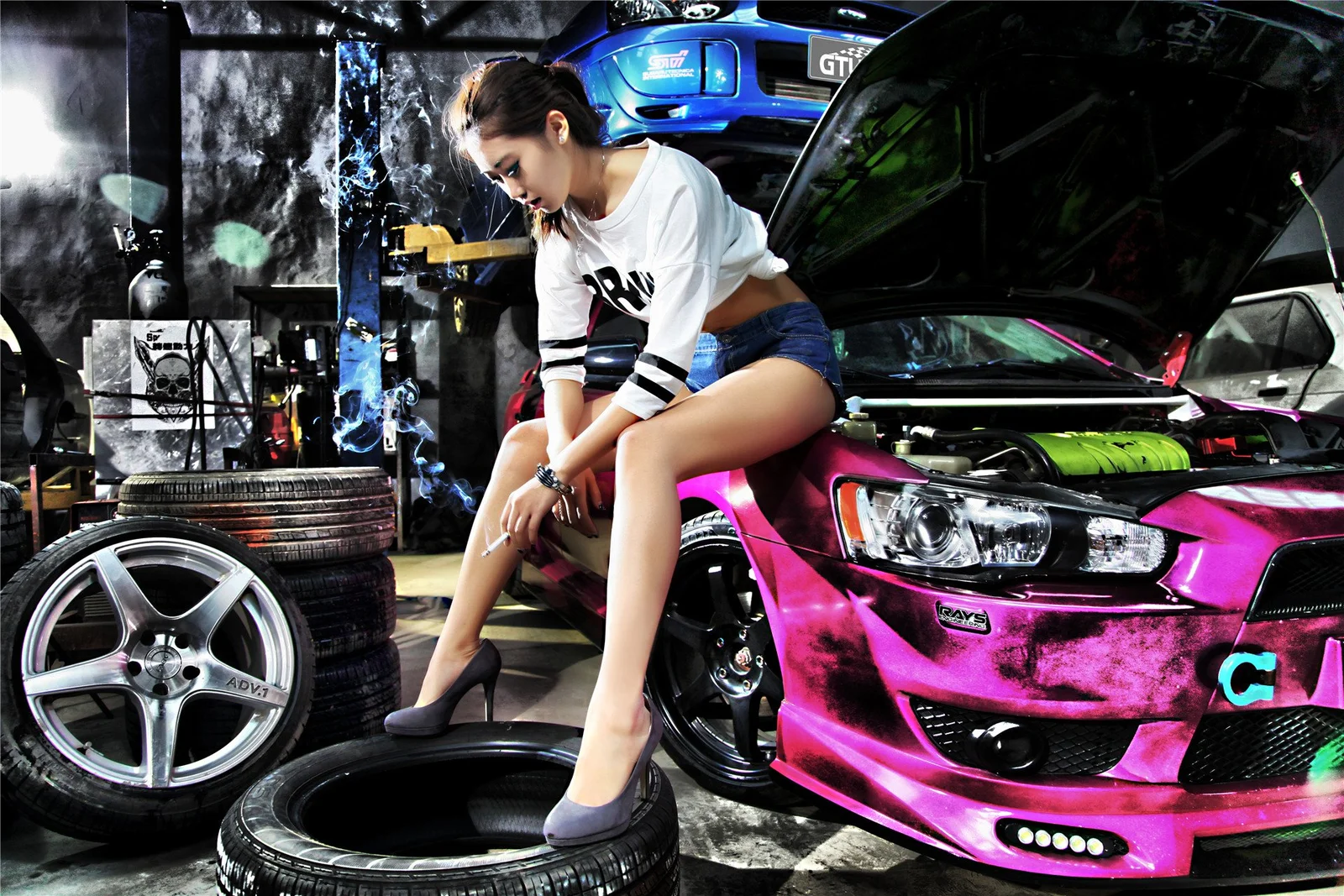一名成年女性坐在車庫內一輛亮粉色跑車旁，周圍可見其他汽車、輪胎和輪圈。