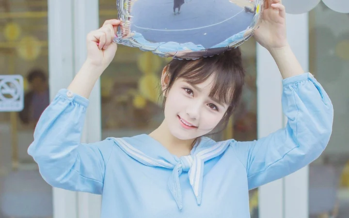 파란 세일러풍 의상을 입은 여성이 창가에서 챙이 넓은 모자를 머리 위로 들고 미소 짓고 있다.