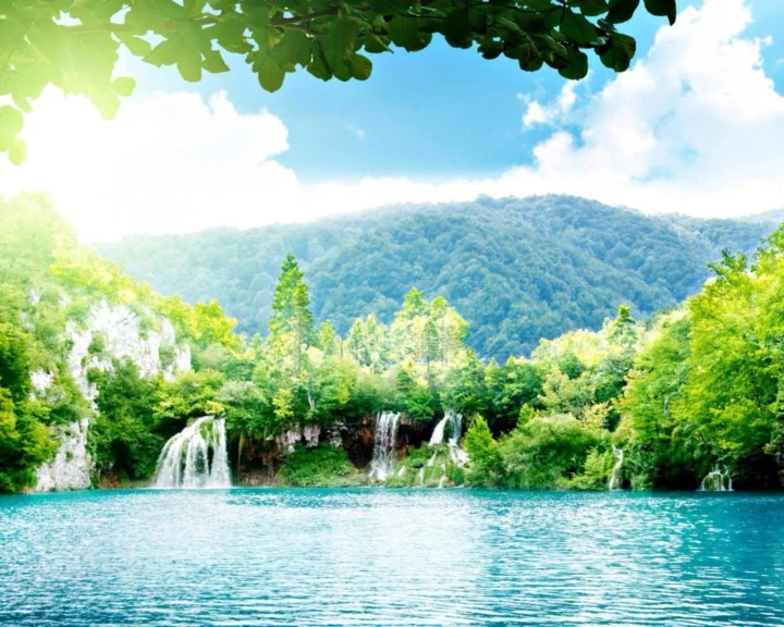 碧蓝湖水前方分布着瀑布、森林和远山，树叶从上方形成自然框景。
