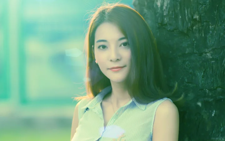 一名成年女子站在树旁，柔和阳光映照着她的面容。