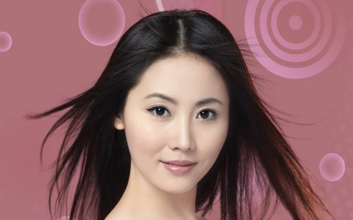 一位长发女性在粉色抽象图案背景前面向镜头微笑。