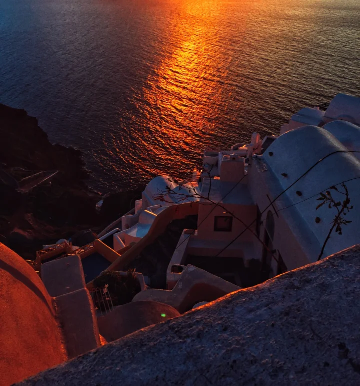 夕阳映照着海面，悬崖上的白色建筑沐浴在暮色与暖光中。