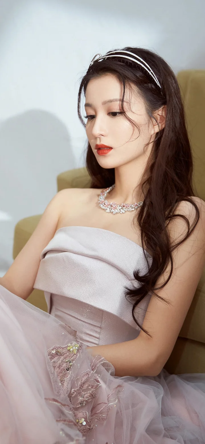 흰색 드레스와 머리띠, 목걸이를 착용한 성인 여성이 실내 의자에 앉아 있습니다.