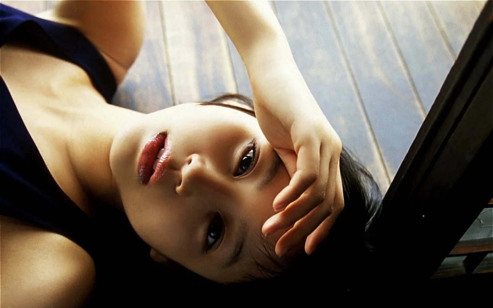 검은 머리의 여성이 화면 속에 옆으로 누워 한쪽 팔을 들고 이마 앞에 손을 둔 채 얼굴을 카메라 쪽으로 향하고 있습니다.