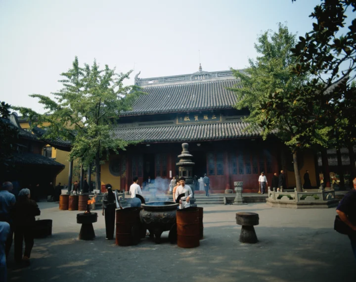 阳光下的古寺建筑面向庭院，前方可见香炉和袅袅烟雾。