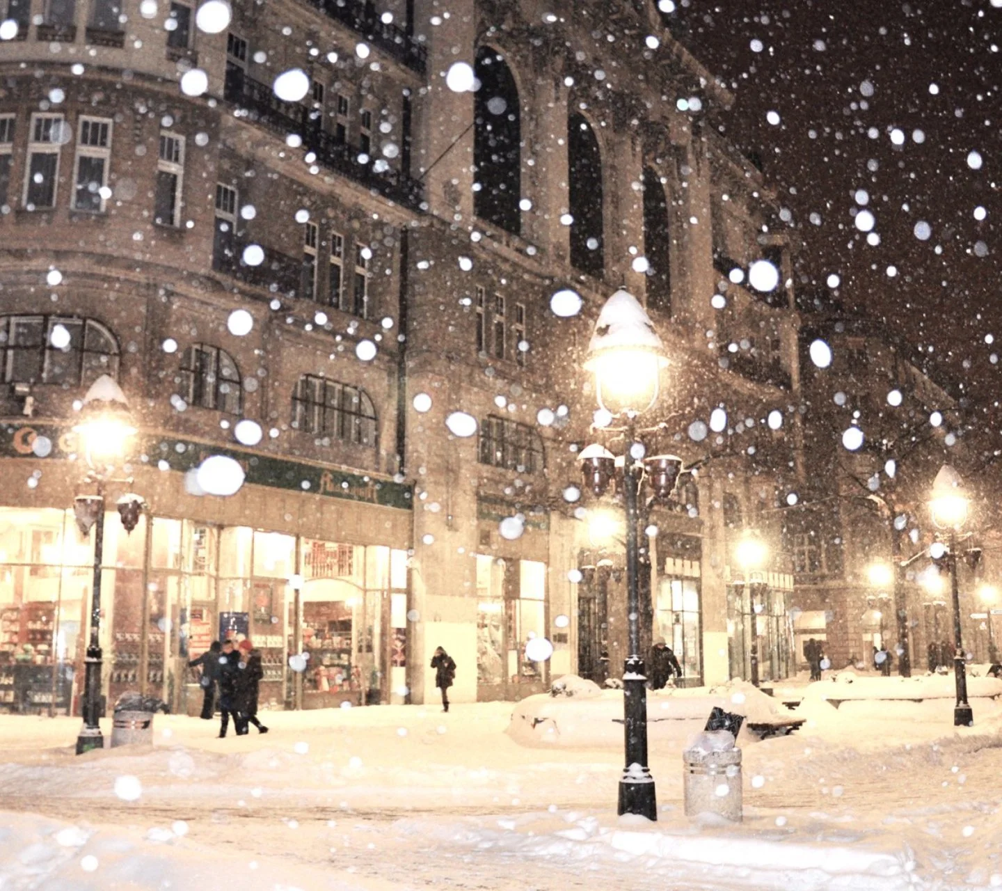 夜の街路が大雪に覆われ、暖かな街灯が歴史的な建物と雪の積もった道を照らしている。