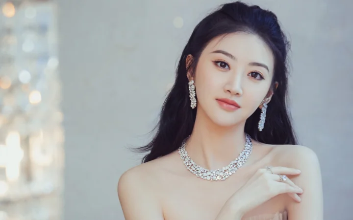 一位佩戴闪亮珠宝的女性面对镜头 posed for a soft studio portrait.