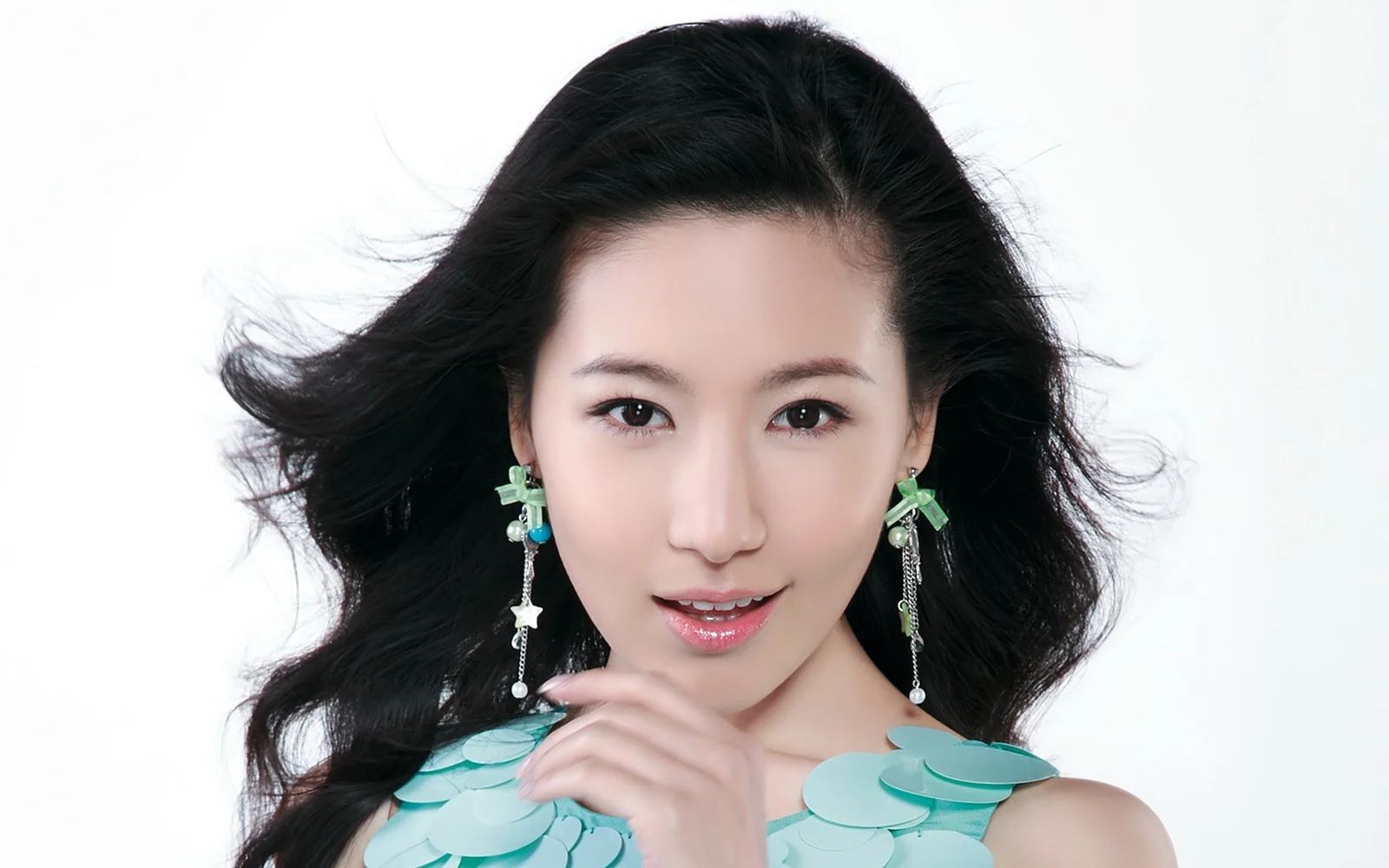 흰색 배경 앞에서 긴 귀걸이를 착용한 검은 머리 여성이 카메라를 향해 미소 짓고 있다.