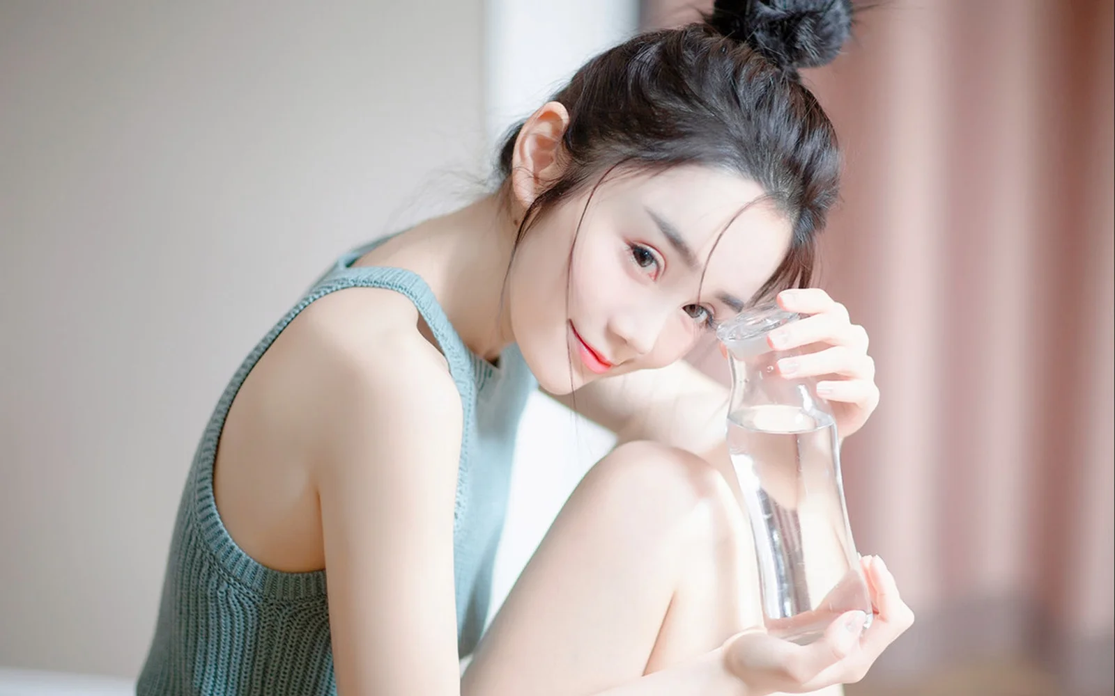 一名成年女性坐在室内，手持透明玻璃杯靠近面部。