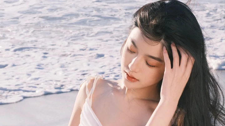 一名成年女性在海边闭眼轻触长发。