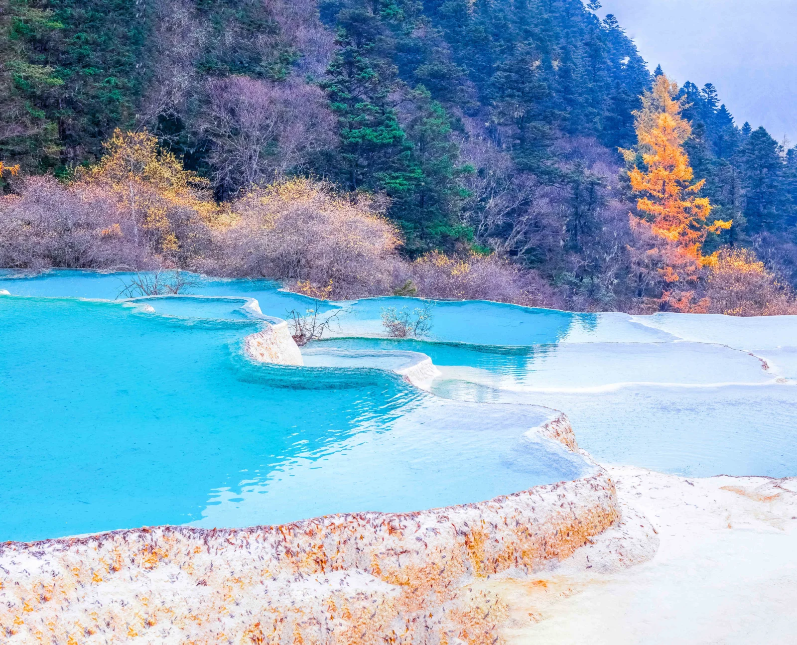 碧藍色的層疊水池坐落在秋色森林與山坡之間。