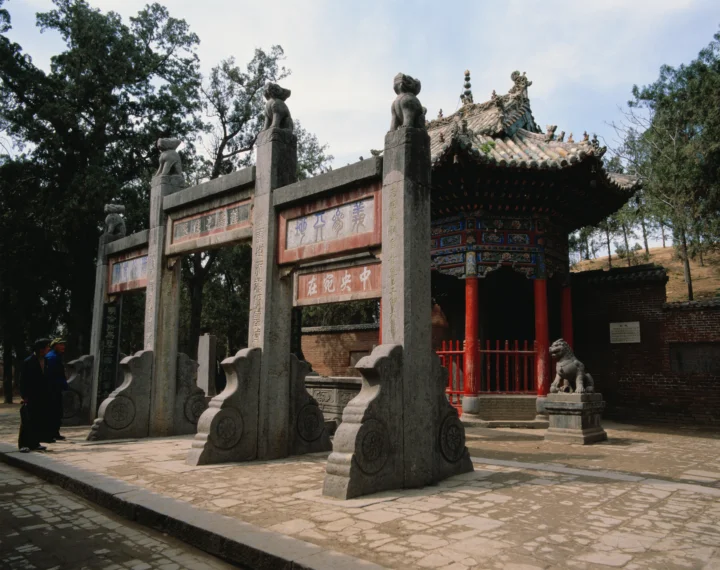 一座雕刻石牌坊矗立在树木环绕的传统中式寺庙前。