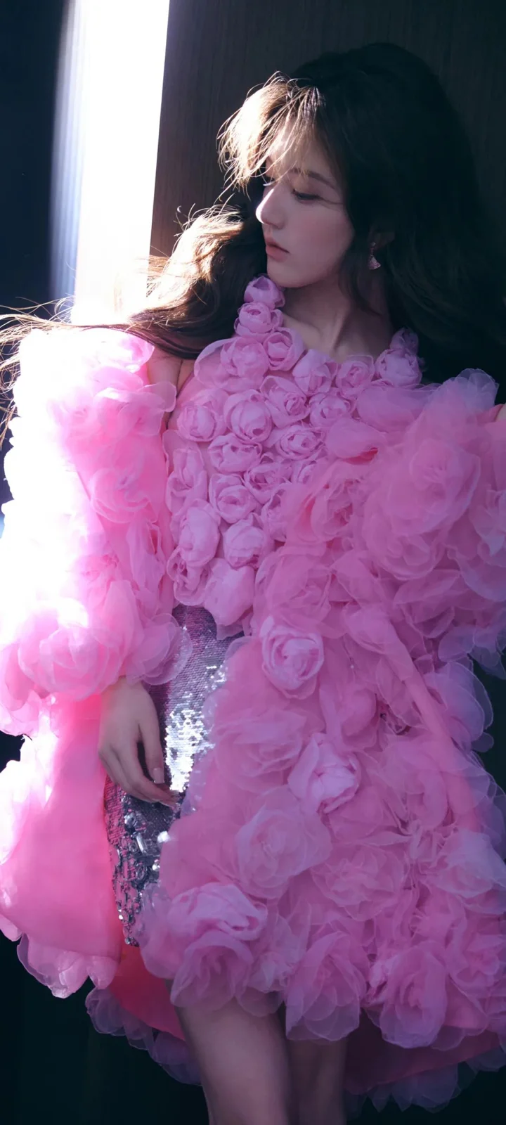 一名成年女性身穿粉色玫瑰装饰礼服，在室内光影中侧头闭目。