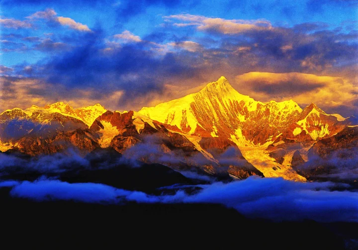 金色夕阳照亮了群山与积雪山峰，浓云在蓝色天空中翻涌。