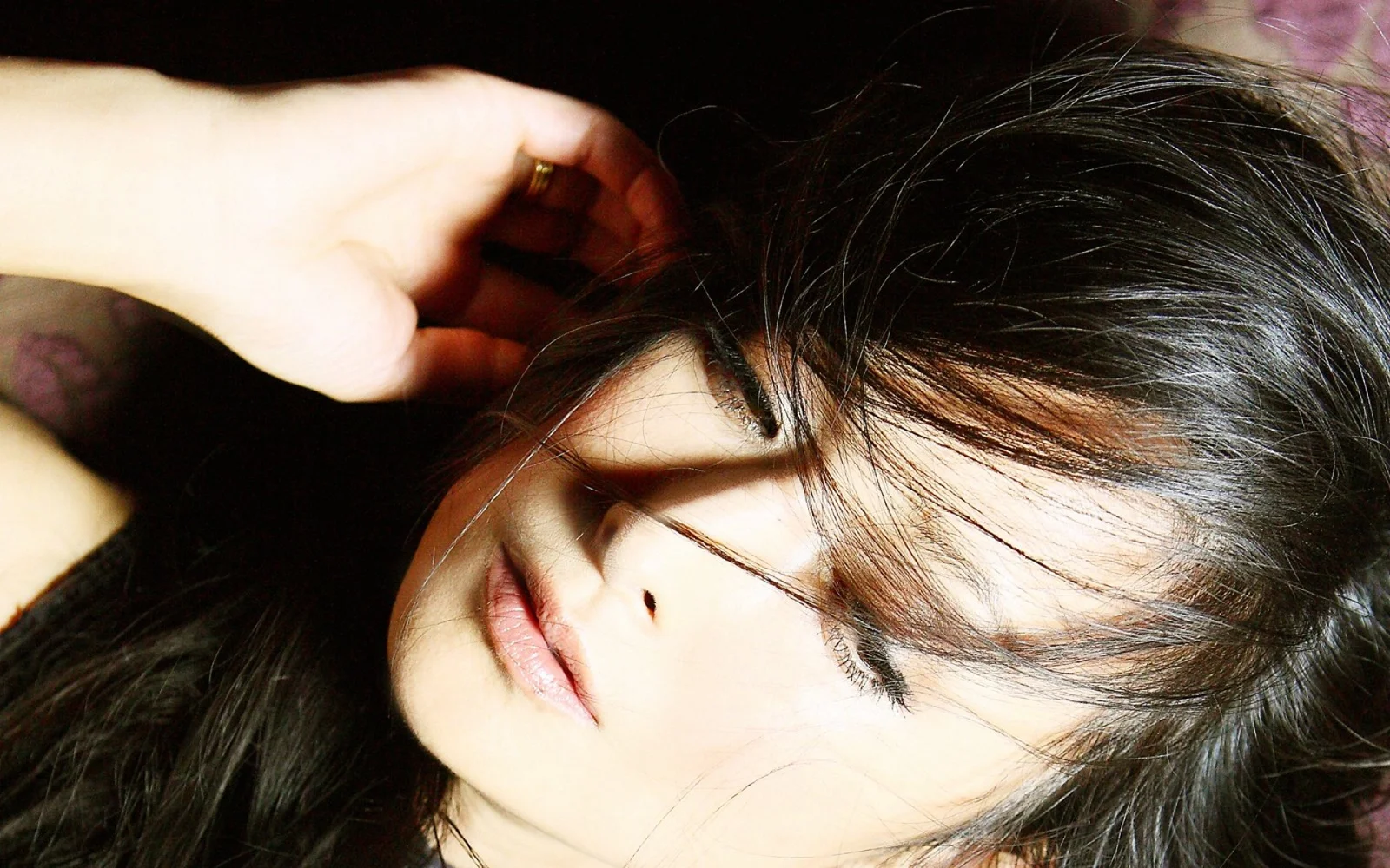 一位黑发成年女性侧躺着闭眼，手臂伸向头部，画面以面部特写为主。