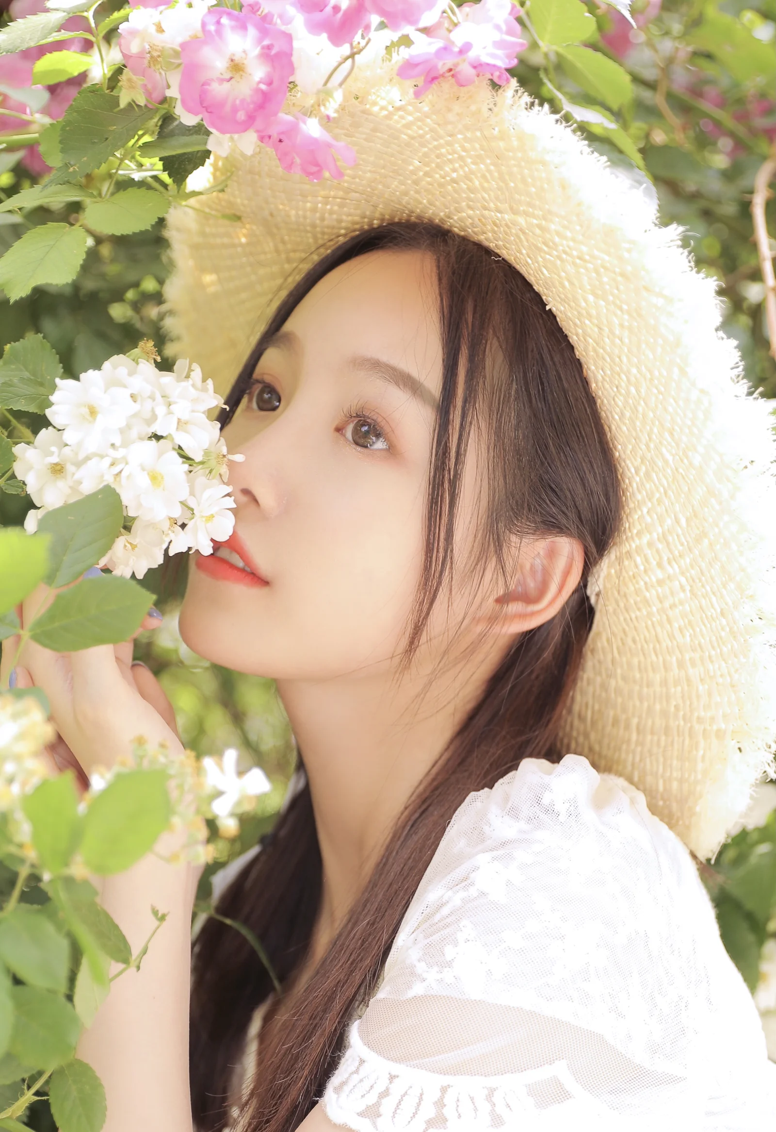 一位戴草帽的女性置身于盛开的花朵和绿叶之间。