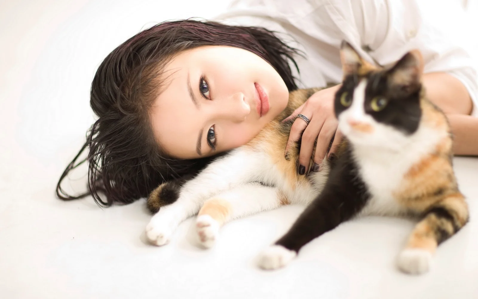 一名女性躺在白色床面上，身旁有两只猫咪。