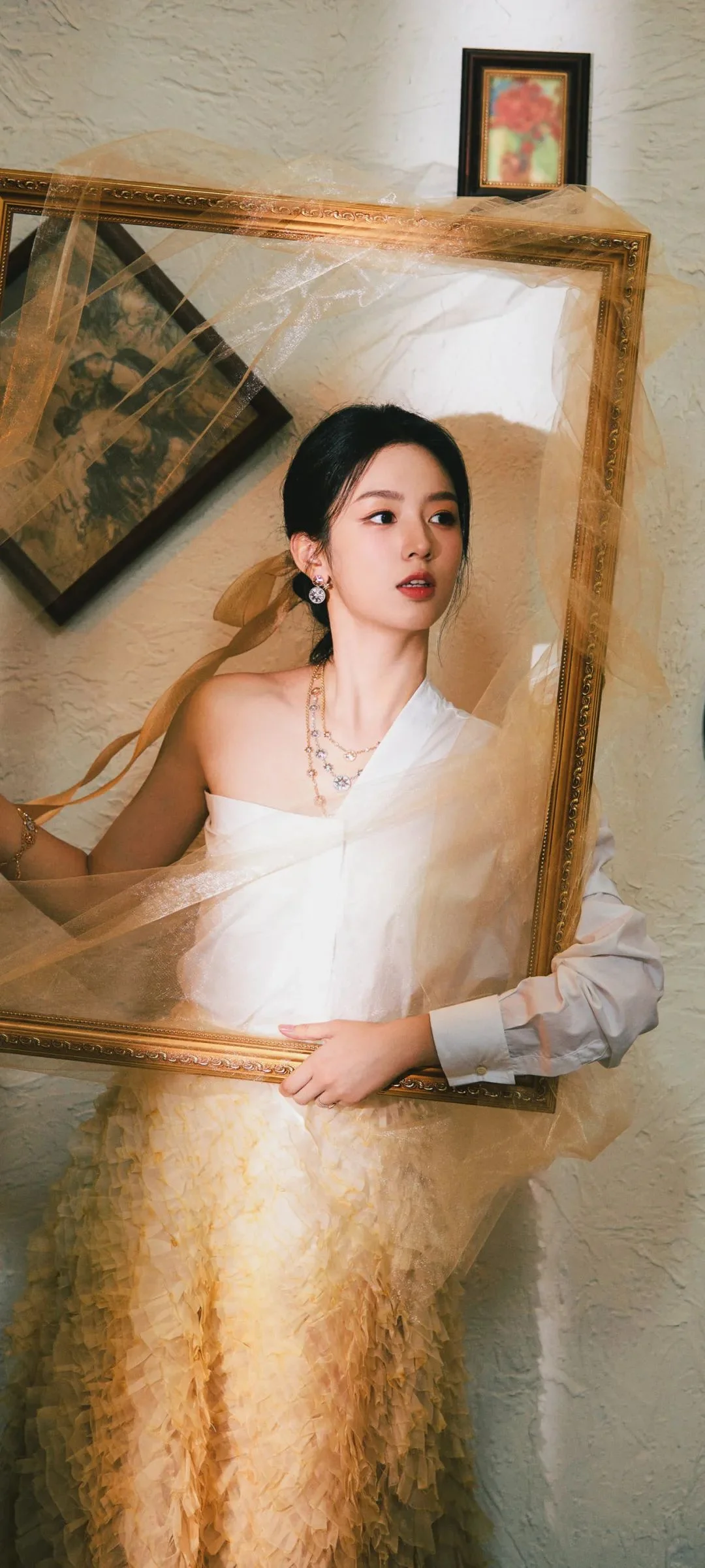 一名身穿白色礼服的女性站在华丽画框前，画面呈现出优雅的室内人像构图。
