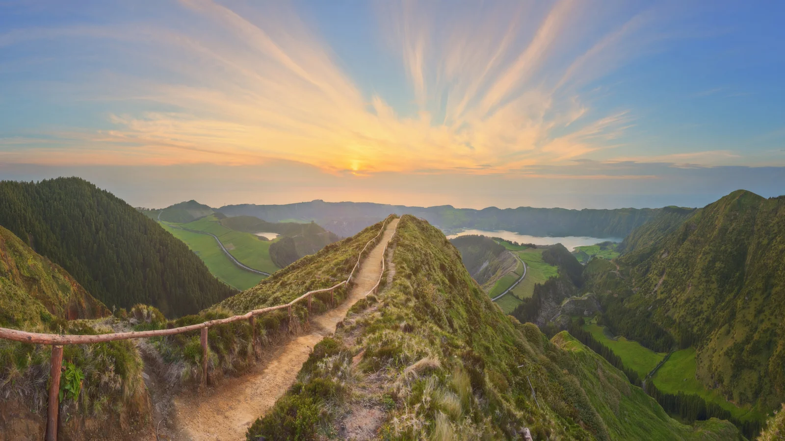 一条山脊步道通向夕阳，四周环绕着绿色山谷与森林。