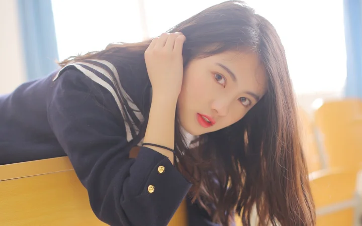 一名长发女性俯身靠在室内桌面旁看向镜头。