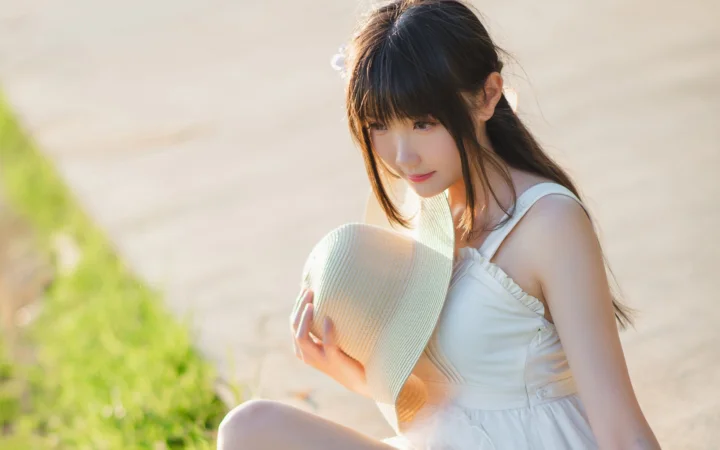 一名身穿白裙的成年女性在户外阳光下手持遮阳帽。