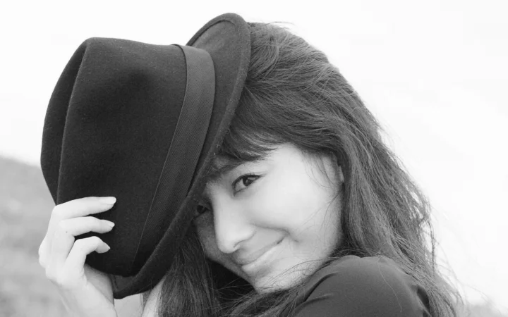 一位戴着宽檐帽的女性面带微笑，构成黑白人像画面。