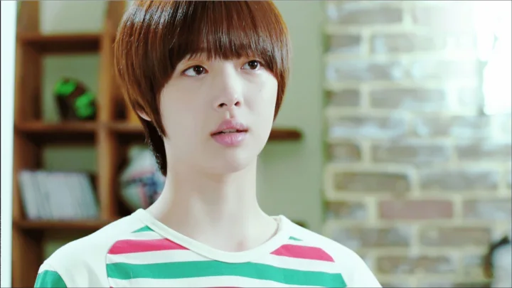 실내에서 단발머리 여성이 카메라를 바라보고 있으며 알록달록한 줄무늬 상의를 입고 있습니다.