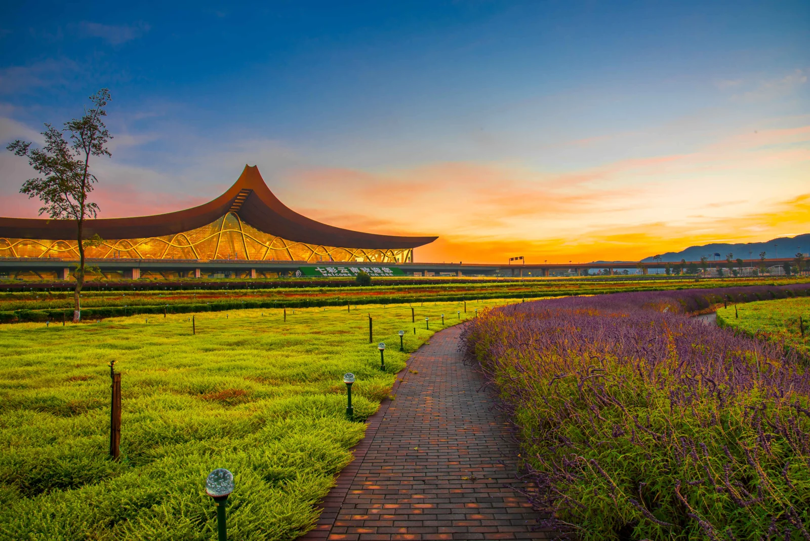 노을빛에 물든 공항 건물과 정원 잔디밭, 멀리 이어지는 벽돌길이 보인다.