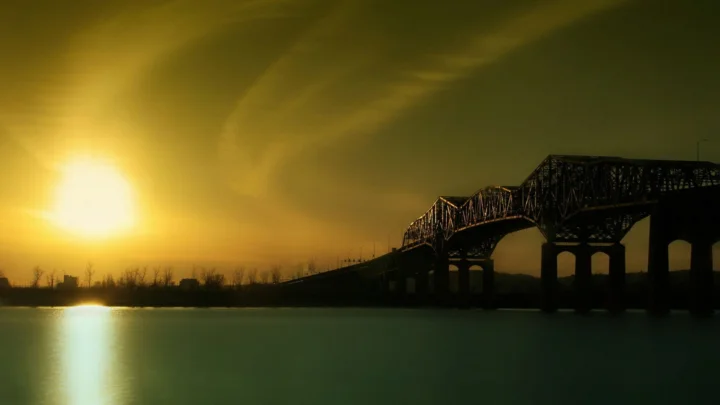 夕阳映照着宽阔水面，远处的钢桁架桥横跨河流，天空呈现金黄色光影。