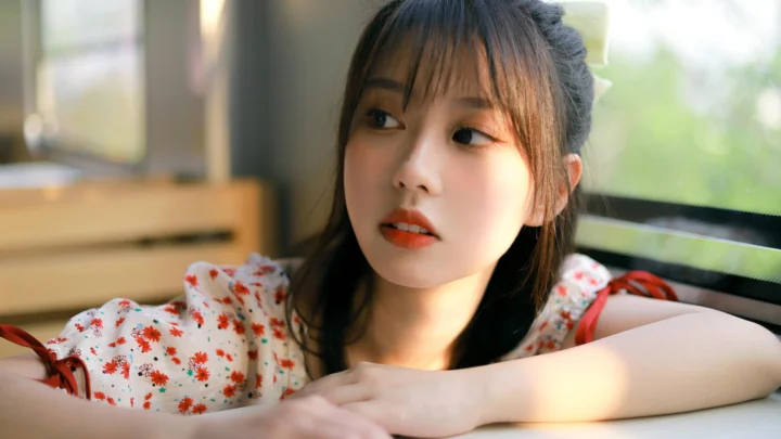 一名身穿碎花上衣的女性靠在窗边，面向一侧望去。
