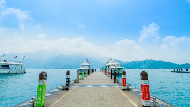 蓝色湖面上的码头通向远处群山，周围停泊着几艘船只。