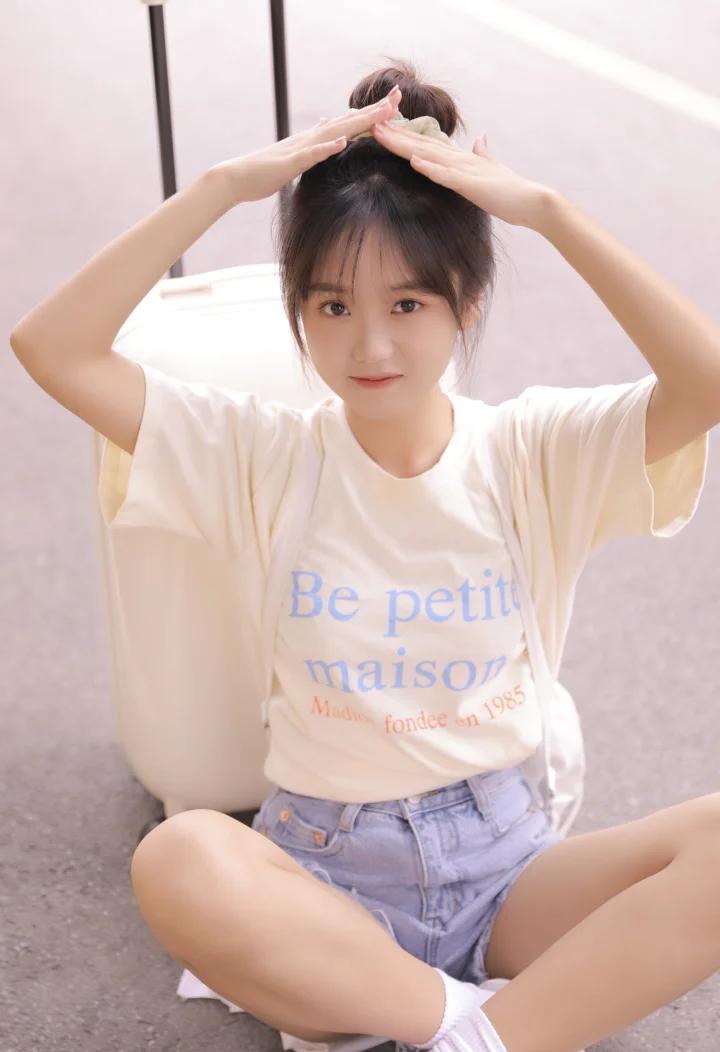 一位扎着高马尾的年轻女子坐在室内，双手举过头顶摆出可爱的姿势。