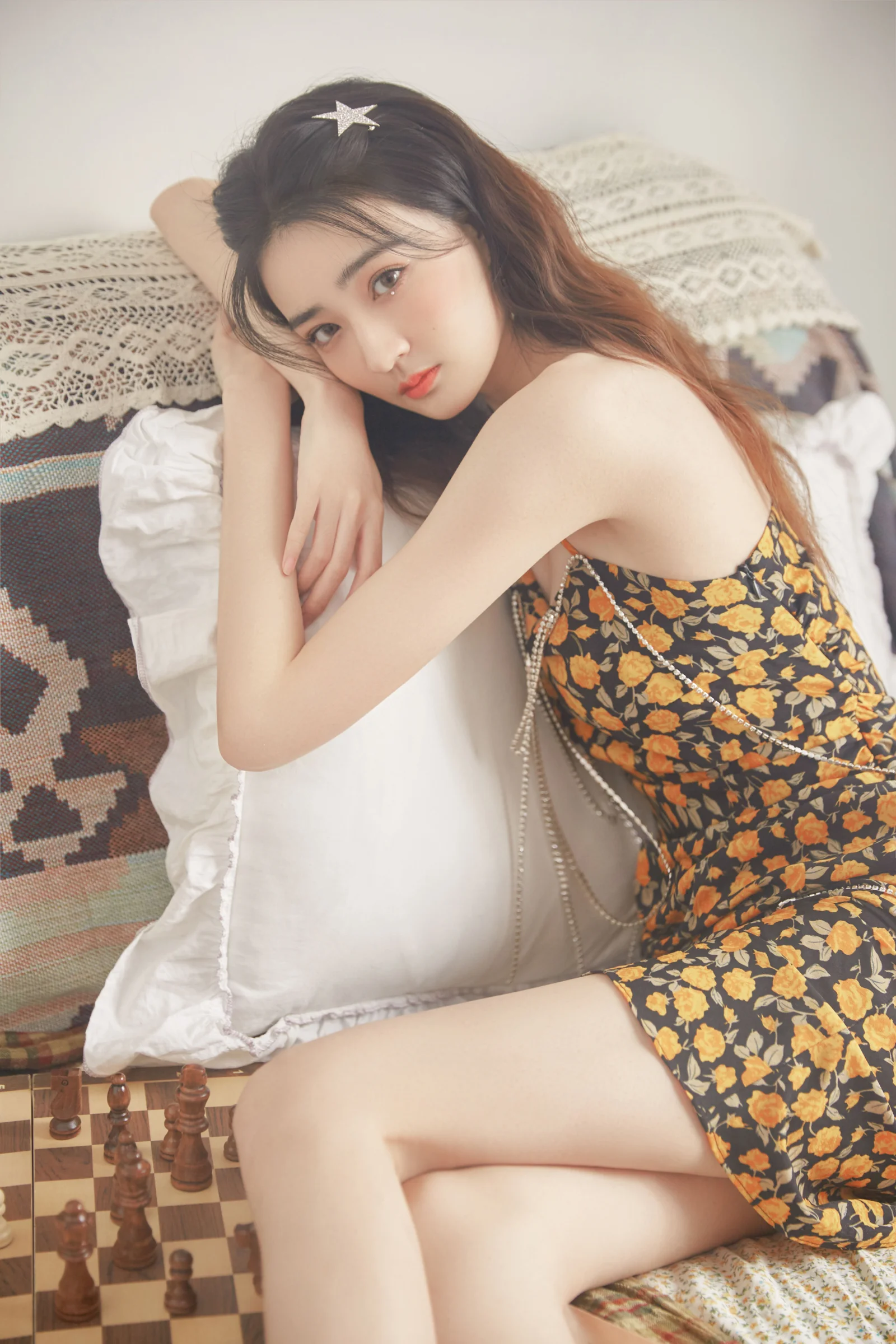 一位成年女子身穿花卉图案连衣裙，倚靠在沙发垫上。