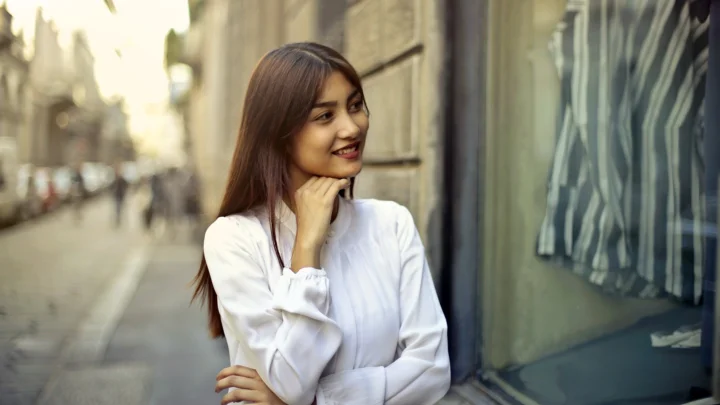 一位身穿白色上衣的成年女子站在城市街道旁微笑。