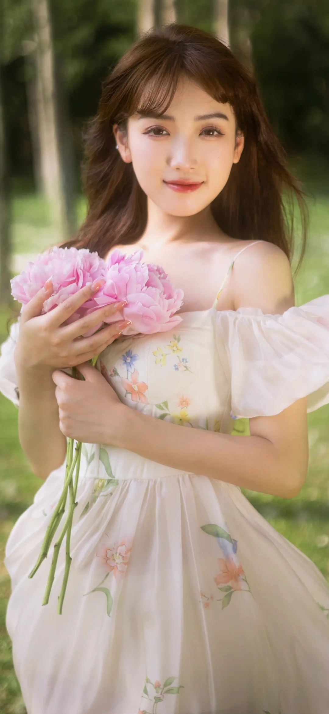 一位成年女性在戶外手捧粉色花束，背景是柔和虛化的樹林。