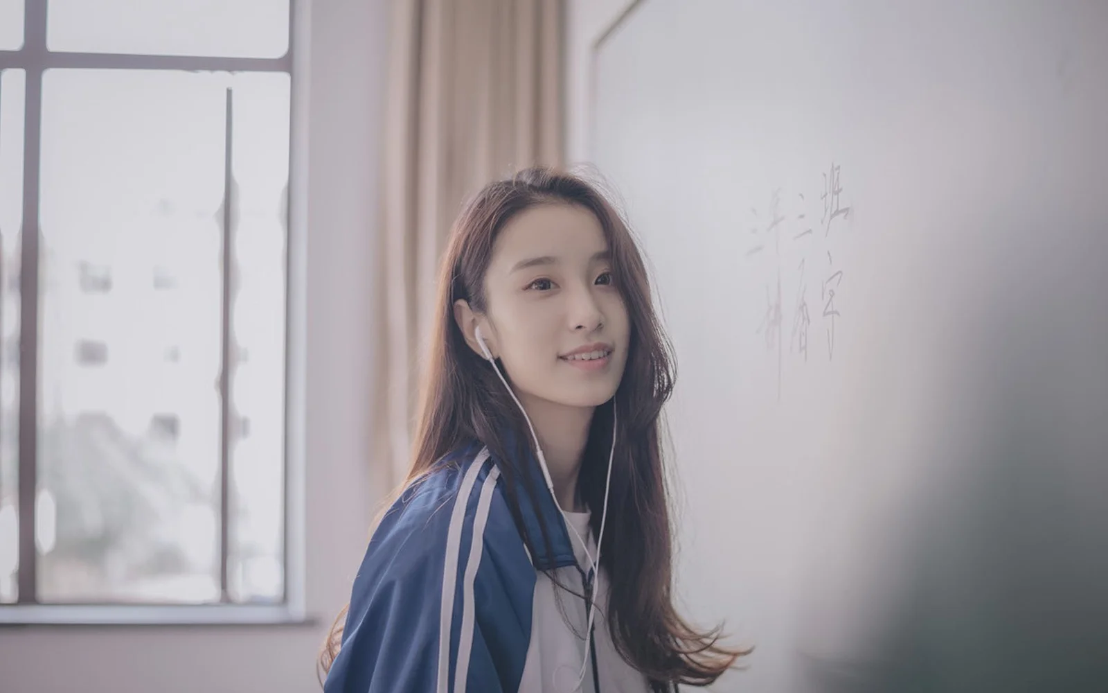 一名戴着有线耳机的女子站在窗边，室内光线柔和。