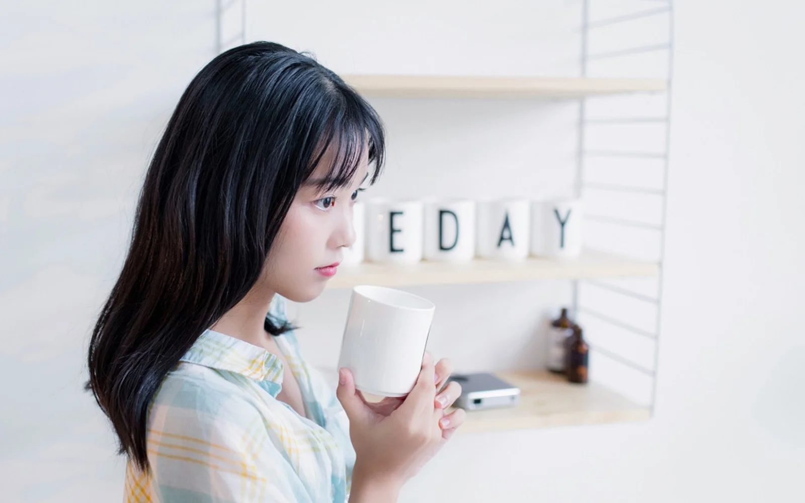 밝은 실내에서 검은 머리의 여성이 흰색 컵을 들고 있다.
