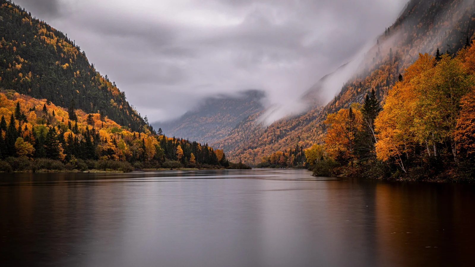 紅葉の森に囲まれた静かな湖の向こうに、霧に包まれた山々が見える。