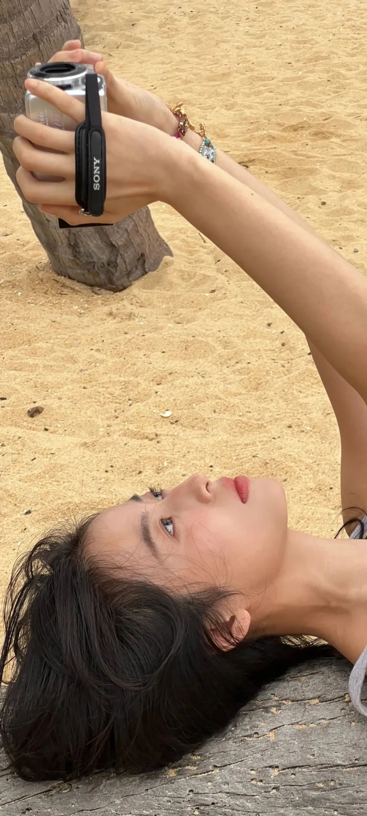 一名女子躺在沙滩上，手边放着相机。