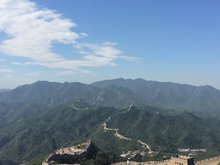 群山与森林环绕的长城蜿蜒穿过山脊，天空中飘着白云。