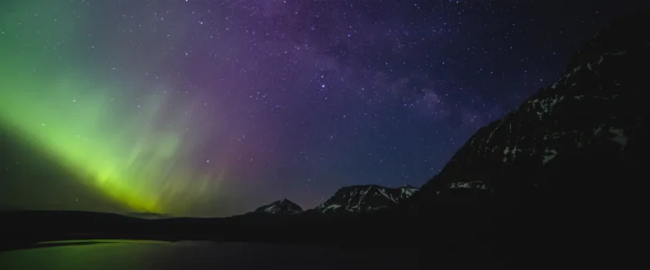 夜空中的绿色极光映照着繁星与远处的山脉剪影。