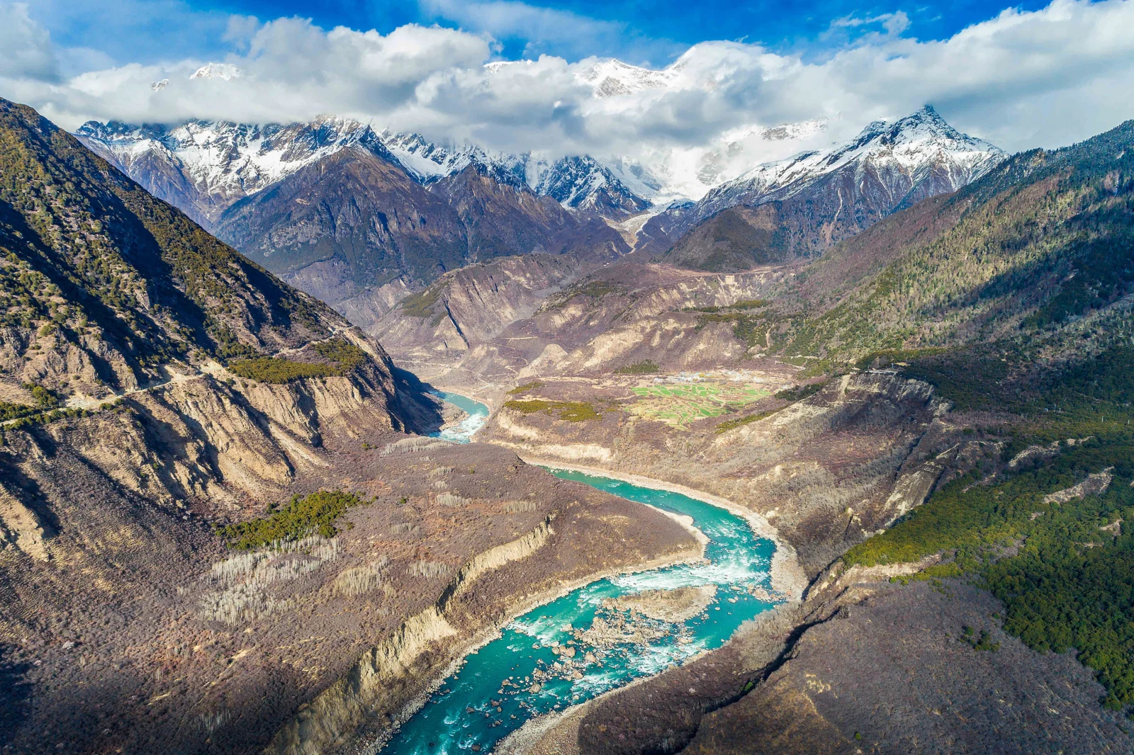 蜿蜒的 turquoise 河流穿过群山峡谷，远处是覆盖积雪的高耸山峰。