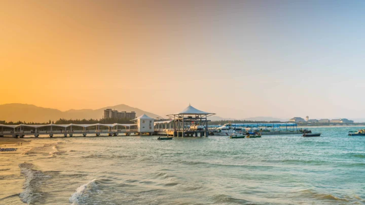 夕阳映照下的海滨码头、海水与远山构成宁静的海岸风景。