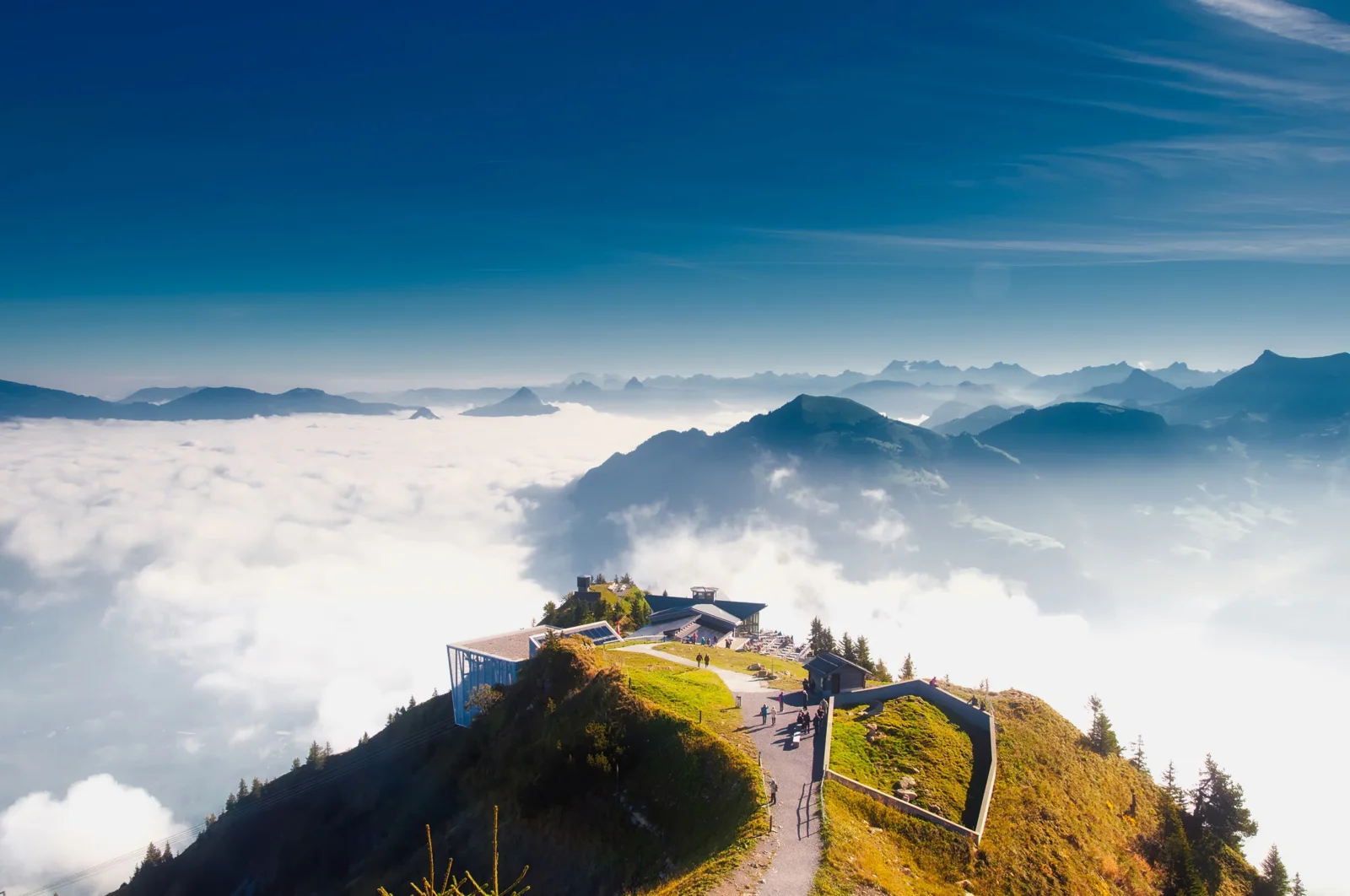 高山观景台和蜿蜒步道坐落在云海之上，远处是层叠的山脉。