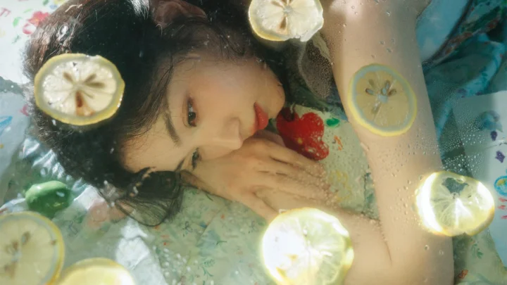 一名女性躺在清澈的水中，周围漂浮着柠檬片和红色水果。