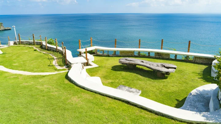 海边的绿色草坪沿着白色步道延伸，远处是开阔的蓝色海面。