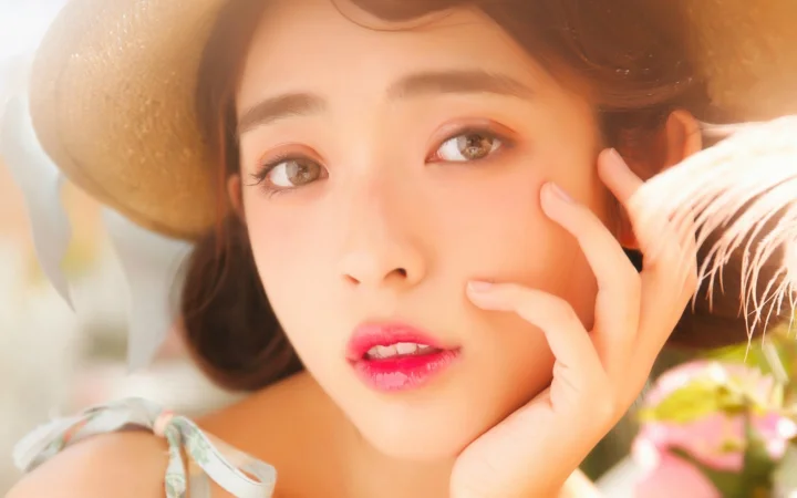 따뜻하고 부드러운 빛 속에서 성인 여성이 카메라를 바라보며 손가락으로 볼을 만지고 있는 클로즈업 인물 사진입니다.