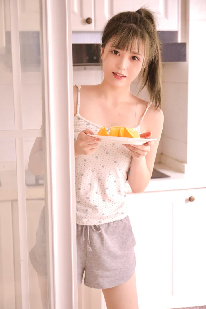明るいキッチンで、若い女性が果物の皿を手に立っている。