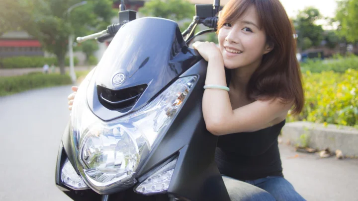一名微笑的女子靠在停在户外道路旁的黑色摩托车上。